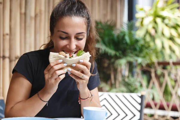 Élelmiszer, blogolás és életmód koncepció. Aranyos európai nő portréja, aki útközben a kávézóban eszik, turista, új ételeket kóstolgat, pitát harap, a hotel éttermében ebédel. — Stock Fotó