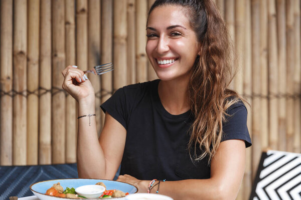 Dining out, breakfast in restaurant and leisure concept. Close-up of beautiful young woman eating alone at cafe table, holding fork and smiling camera, trying Bali cuisine, enjoying vacation Stock Picture