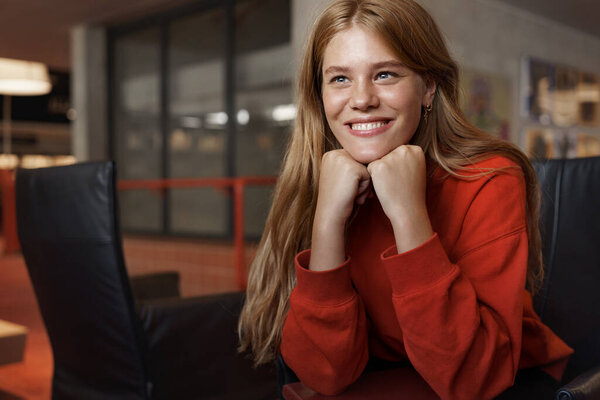 Close-up of dreamy redhead girl student, sit armchair, lean head on hands and looking away with pleased, thoughtful smile, finished reading good novel, new bestseller in library, studying for exam Royalty Free Stock Images