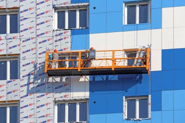 İnşaatçılar çok yönlü bir ön cepheye beyaz ve mavi paneller kurarlar-