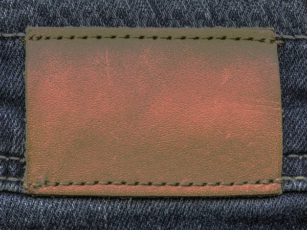 Červeno šedý kožený štítek na pozadí džínovina — Stock fotografie