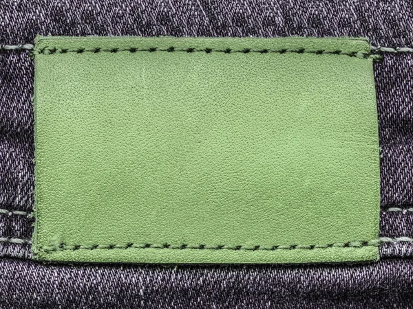 Светло-зеленая кожаная этикетка на джинсовом фоне — стоковое фото