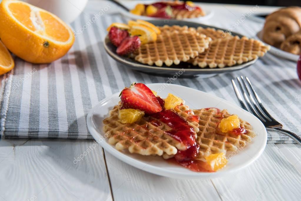Close-up view of fresh homemade waffles with fruits and jam on table