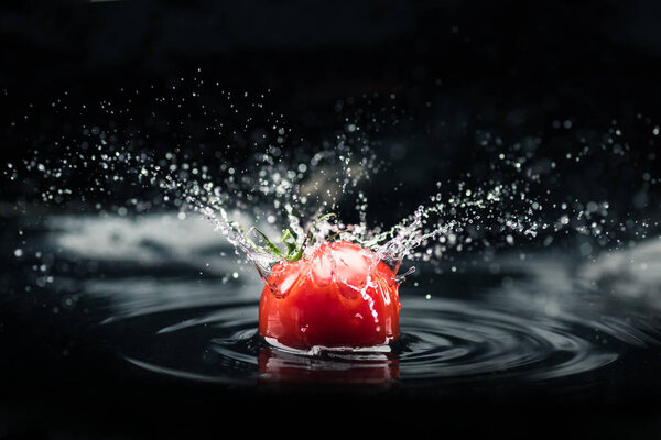 Свежий помидор падает в воду
