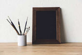 photo frame and paintbrushes on tabletop