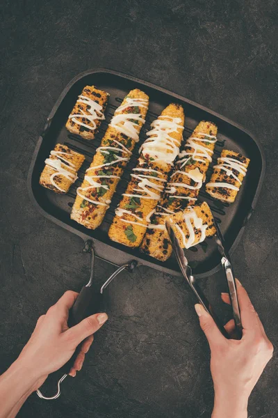Woman taking grilled corn from pan — Stock Photo, Image