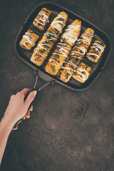 woman holding grill pan with corn