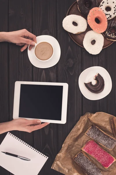 Pessoa com café, tablet digital e donuts — Fotografia de Stock