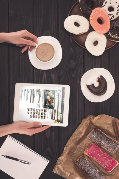 Person med kaffe, digital tablett och munkar — Stockfoto