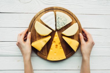 hands and wooden board with assorted cheese