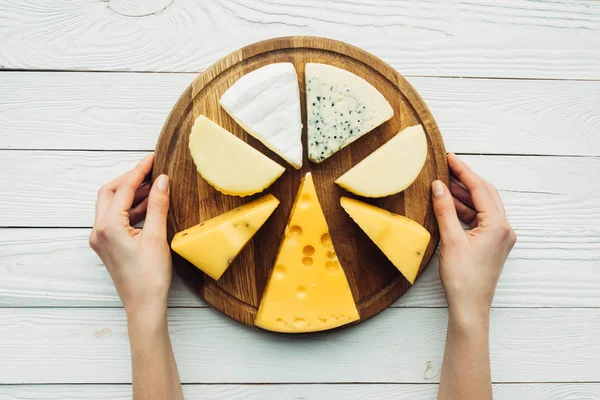 Manos y tabla de madera con queso surtido — Foto de Stock