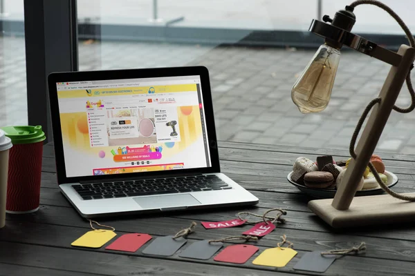 Laptop mit aliexpress-Website auf Tisch mit Macarons, Kaffee- und Verkaufsanhängern im Café — Stockbild Laptop mit aliexpress-Website — Stockfoto