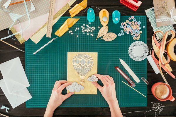 cropped image of designer adding clouds to scrapbooking handmade postcard