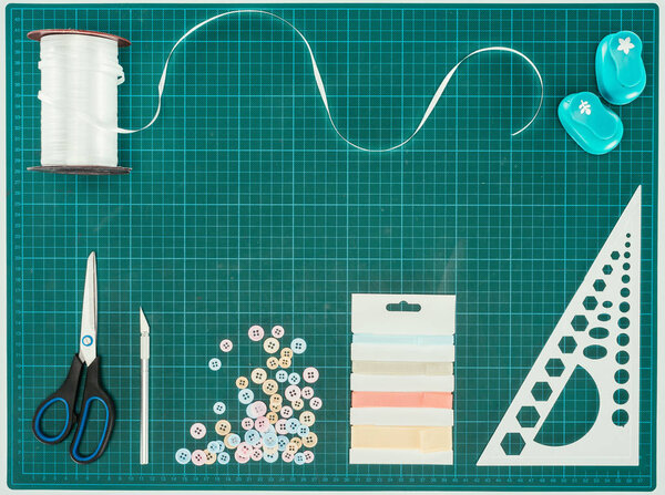 Вид сверху ножниц, пуговиц и лент для украшения шрапбукинга в бирюзовой гамме
