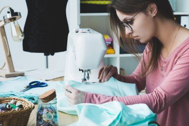 Genç terzi dikiş makinesi işyerinde kullanarak yan görünüm