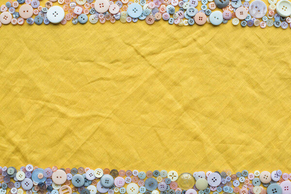 top view of colorful buttons frame on yellow cloth background with copy space