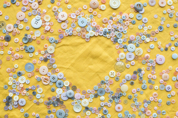 top view of colorful buttons heart shaped frame on yellow cloth background with copy space