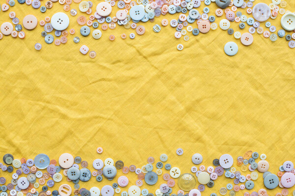 top view of colorful buttons frame on yellow cloth background with copy space