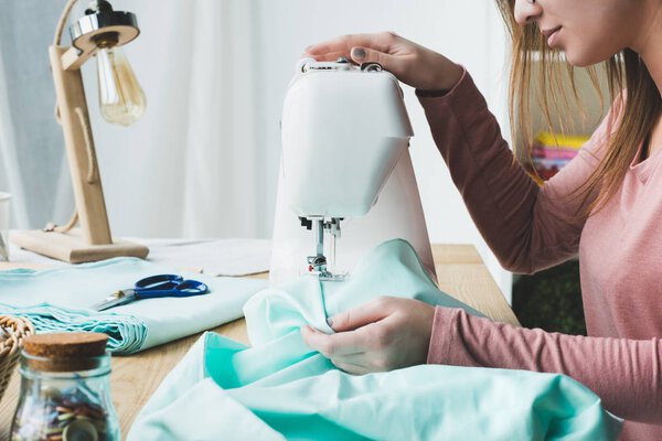 cropped image of young seamstress using sewing machine at workplace