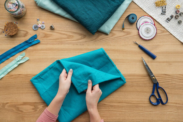 верхний вид обрезанных женских рук складывая ткань на рабочем месте швеи с ножницами и кнопками
