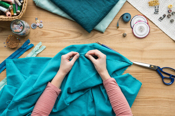 верхний вид обрезанных женских рук, швейная ткань с иглой на рабочем месте швеи

