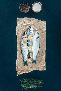 top view of healthy organic fish with lemon slices on baking paper on black clipart