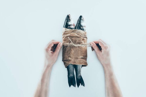 partial view of hands wrapping sea fish in paper and tying with rope on grey