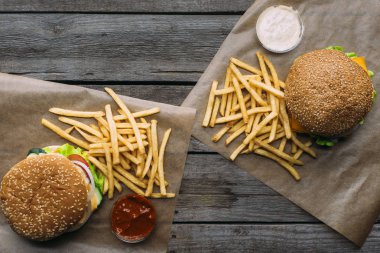 ahşap masa üzerinde kagit üzerinde üstten görünüm hamburger, patates kızartması ve soslar