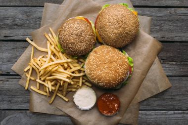 ahşap masa üzerinde kagit üzerinde üstten görünüm hamburger, patates kızartması, ketçap ve mayonez