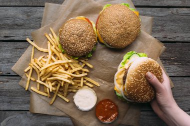 Üstten Görünüm hamburger, patates kızartması ve soslar ile el ahşap masa üzerinde kagit üzerinde