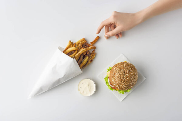 обрезанный вид женской руки с картошкой фри, домашний гамбургер и майонез, изолированные на белом
