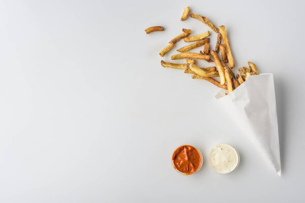 top view of french fries in paper cone, mayonnaise and ketchup sauces, isolated on white