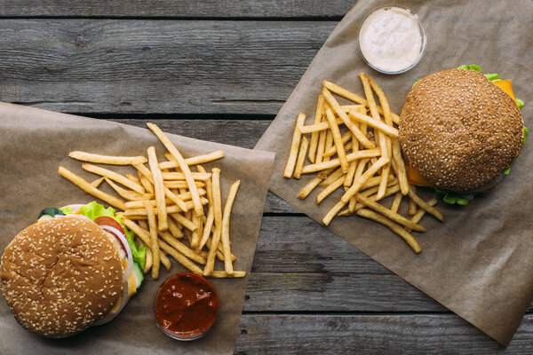 top view of hamburgers, french fries and sauces on baking paper on wooden tabletop