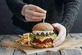 oříznutý pohled ženské ruce velké chutné cheeseburger a hranolky na pečícím papírem