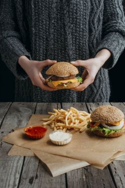 patates kızartması ve soslar ile masada çizburger ve standig tutan kadın görünümünü kırpılmış