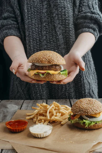 Cropped View Woman Holding Cheeseburger Standig Table French Fries Sauces — Stock Photo, Image