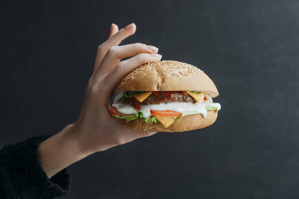 cropped view of hand with gourmet homemade cheeseburger on black