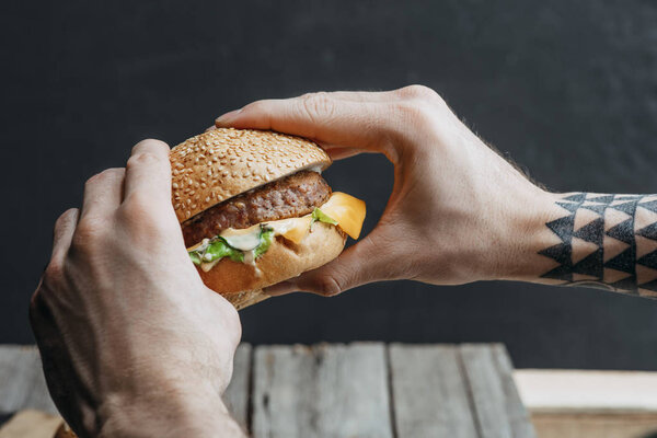 cropped view of man holding tasty homemade cheeseburger