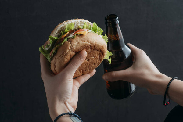 обрезанный вид человека с гамбургером и бутылкой пива
