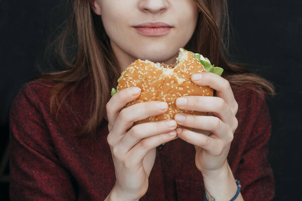 cropped view of girl eating tasty cheeseburger