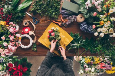 cropped image of female florist wrapping bouquet in pack paper clipart