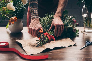 cropped image of florist with tattoo on hand cutting stalks with pruner clipart