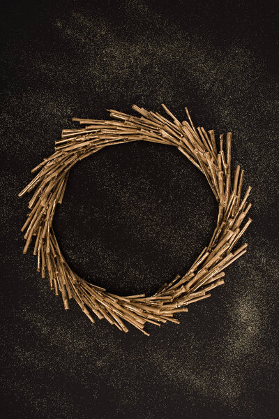 top view of golden wreath made of sticks on black surface