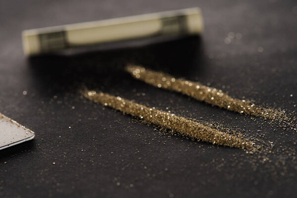 selective focus of golden powder lines and dollar on black surface