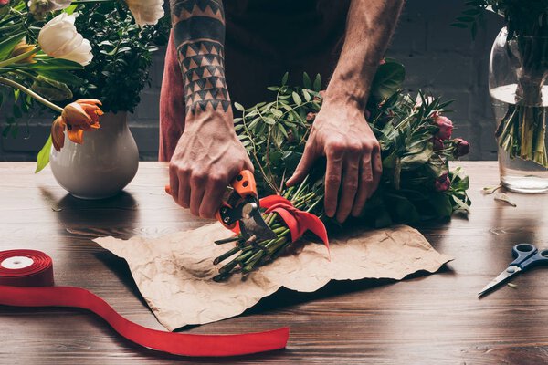 cropped image of florist with tattoo on hand cutting stalks with pruner