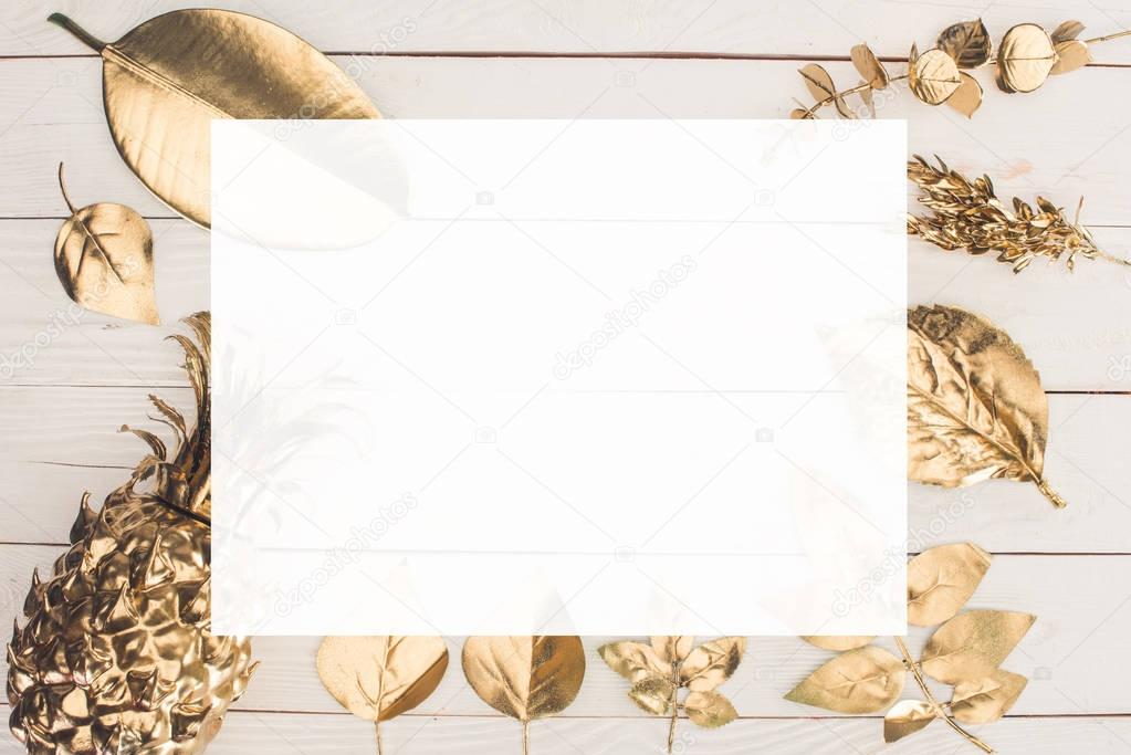 top view of colored in golden various leaves and pineapple with blank paper in middle on wooden tabletop