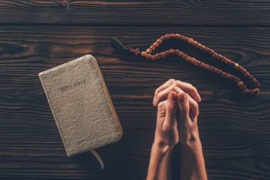 cropped image of woman sitting at table with rosary and holy bible and praying   clipart