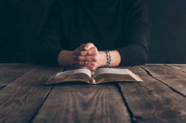 cropped image of woman sitting at table with rosary and bible and praying  