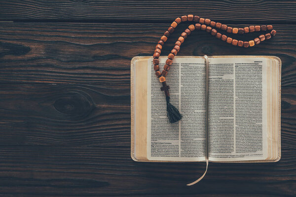 top view of open holy bible with rosary on wooden table 