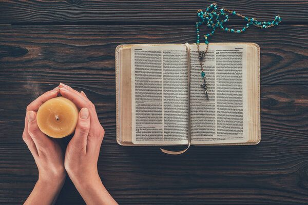 cropped image of woman holding candle above wooden table with bible